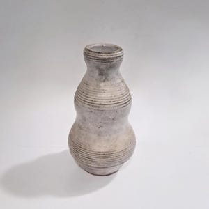 May include: A handcrafted ceramic vase with a unique gourd shape. The vase features horizontal, textured lines and a speckled, muted color palette of gray, white, and beige. The vase is a decorative item for the home.