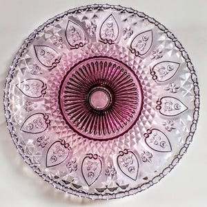 Pu&ograve; includere: Un piatto da portata rotondo in vetro vintage con un design decorativo. Il piatto presenta un cerchio centrale magenta scuro circondato da un'area rosa pi&ugrave; chiara con motivi a forma di foglia. Il bordo ha un bordo strutturato e perlato. Per servire cibo.