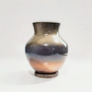 May include: A handcrafted ceramic vase with a gradient finish. The vase transitions from a dark brown at the top to a deep blue-purple in the middle, and finally to a copper-orange at the base. The vase has a rounded body and a slightly flared neck.