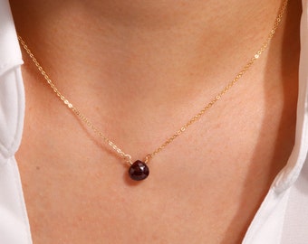 May include: A delicate gold chain necklace with a small, dark red gemstone pendant.
