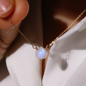 May include: A delicate gold chain necklace with a single iridescent moonstone pendant.
