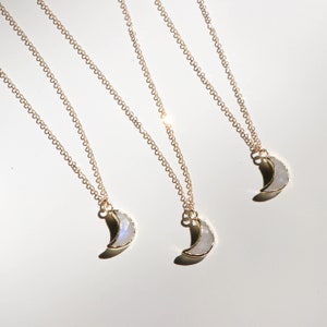 Puede incluir: Tres collares de oro con colgantes de media luna hechos de piedra lunar blanca. Los collares est&aacute;n superpuestos sobre un fondo blanco.
