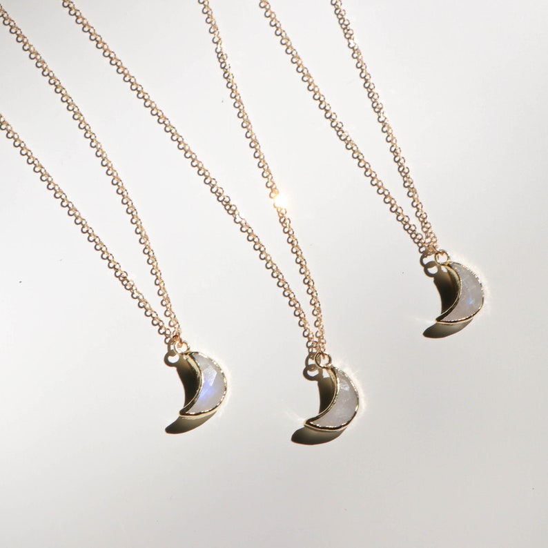 Puede incluir: Tres collares de oro con colgantes de media luna hechos de piedra lunar blanca. Los collares est&aacute;n superpuestos sobre un fondo blanco.