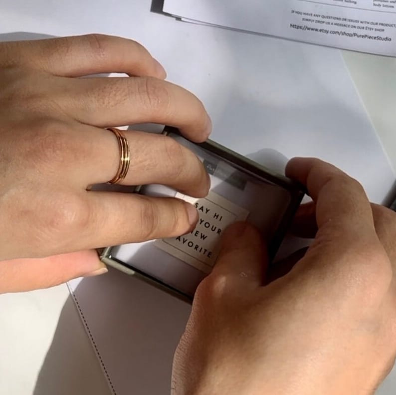 Puede incluir: Una peque&ntilde;a caja blanca con un borde dorado. La caja est&aacute; abierta y una peque&ntilde;a tarjeta en el interior dice "Saluda a tu nuevo favorito".