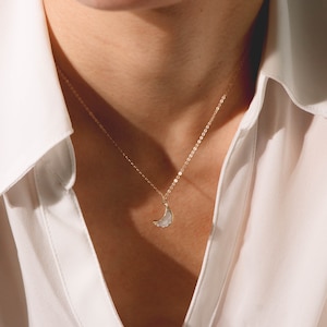 Puede incluir: Un collar de cadena dorada con un colgante de media luna. El colgante est&aacute; hecho de piedra blanca.
