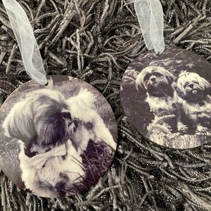May include: Two round ornaments with black and white photos of dogs. One ornament features a single dog with a bow tie, while the other ornament features two dogs.