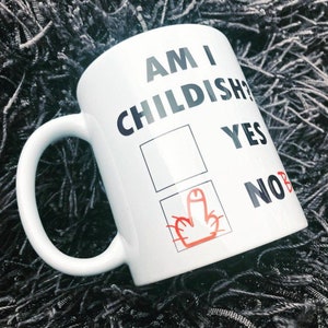K&ouml;nnte beinhalten: Wei&szlig;e Keramiktasse mit schwarzem Text, der "Am I Childish?" lautet, mit einem Kontrollk&auml;stchen und den W&ouml;rtern "Yes" und "No" daneben. Das K&auml;stchen "No" ist angekreuzt, mit einem roten Mittelfinger, der darin gezeichnet ist.
