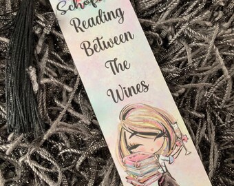 Könnte beinhalten: Ein farbenfrohes Lesezeichen mit einem Blumendesign und einem schwarzen Quasten. Das Lesezeichen zeigt eine Comic-Illustration einer Frau, die einen Stapel Bücher und ein Glas Wein hält. Der Text auf dem Lesezeichen lautet "Miss Schofield Reading Between The Wines".