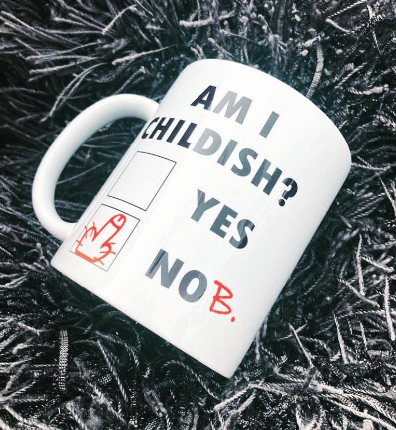K&ouml;nnte beinhalten: Wei&szlig;e Keramiktasse mit dem Text "Am I Childish?" und einem Kontrollk&auml;stchen mit zwei Optionen: "Yes" und "No B." Die Option "No" ist mit einem roten Mittelfinger angekreuzt.