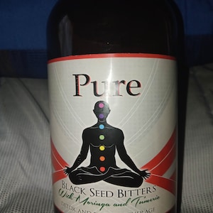 Könnte beinhalten: Eine Glasflasche mit einem schwarzen Etikett, auf dem "Pure Black Seed Bitters With Moringa and Turmeric Detox and Energy Beverage" steht. Das Etikett zeigt auch eine schwarze Silhouette einer Person, die in einer Yoga-Pose sitzt, mit bunten Kreisen, die die Chakren darstellen.
