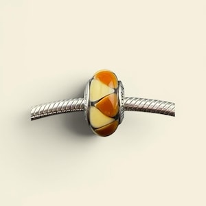 May include: A glass bead with a silver core. The bead is cylindrical, featuring a pattern of orange and cream-colored segments. The bead is strung on a silver chain. The word "Pandora" is visible on the bead.