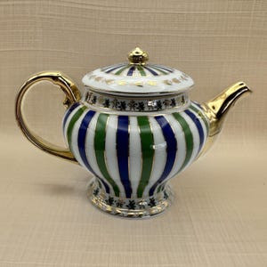 May include: A decorative porcelain teapot with a gold handle, spout, and accents. The teapot features vertical stripes in blue, green, and white. The lid is white with blue and green stripes and a gold finial. The base has a gold trim.