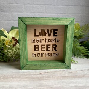 May include: A wooden sign with a green frame and the text "LOVE in our hearts BEER in our bellies!" with a shamrock symbol.