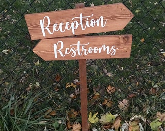 Könnte beinhalten: Holzschilder mit weißem Text, die auf den Empfang und die Toiletten zeigen. Das Schild ist braun und hat einen rustikalen Look.