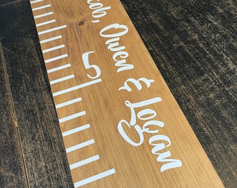 May include: A wooden growth chart with white markings and the names "Jacob, Owen & Logan" written in white cursive lettering.