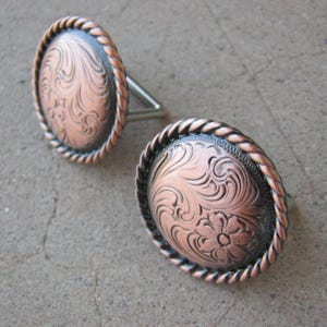 May include: Two copper-colored metal conchos with a rope-like border and an engraved floral design.