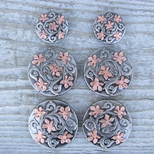 May include: Six silver and copper floral conchos with a swirling design. The conchos are round and have a raised design of flowers and leaves.