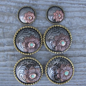 May include: Set of five silver and gold concho buttons with a floral design. The center of each flower is a light green stone, and the petals are a copper color.