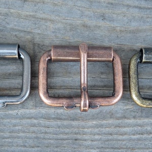 May include: Three metal belt buckles in different finishes: silver, copper, and brass. Each buckle has a rectangular shape with a smooth, polished surface.