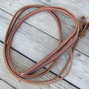 May include: A pair of brown leather reins with stitching detail. The reins are folded and coiled together.