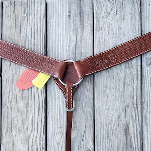 May include: A brown leather horse breast collar with decorative tooling and white stitching. The breast collar has a basket weave pattern and floral designs. It features adjustable straps and metal hardware.