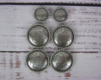 Op de afbeelding: Vijf zilverkleurige metalen knopen met een touwachtige rand en een gegraveerd bloemenmotief.