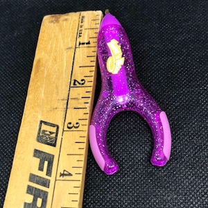 May include: Purple glitter pen shaped like a rocket with a yellow Hot Wheels logo. The pen is about 3 inches long.