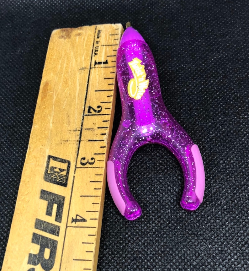 May include: Purple glitter pen shaped like a rocket with a yellow Hot Wheels logo. The pen is about 3 inches long.
