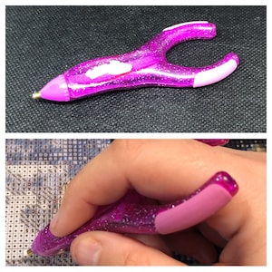 May include: A pink diamond painting pen with a clear plastic handle and a rubber grip. The pen has a small metal tip for picking up diamonds.