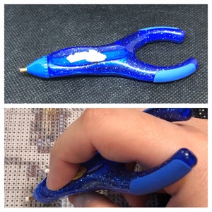 May include: Blue diamond painting pen with a clear plastic body and a blue rubber grip. The pen has a small metal tip for picking up diamonds.