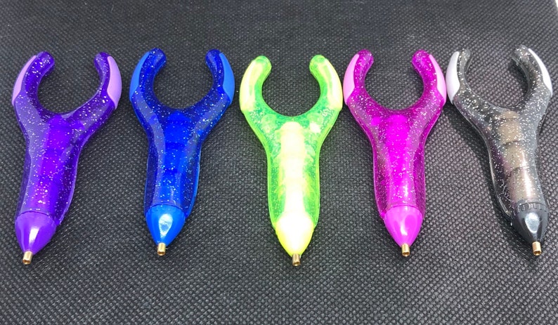 May include: Five colorful pens with glitter and a unique ergonomic design. The pens are purple, blue, green, pink, and black.