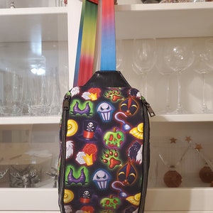 May include: A black crossbody bag with a colorful print of various Disney villains' icons. The bag has a rainbow and blue adjustable strap.