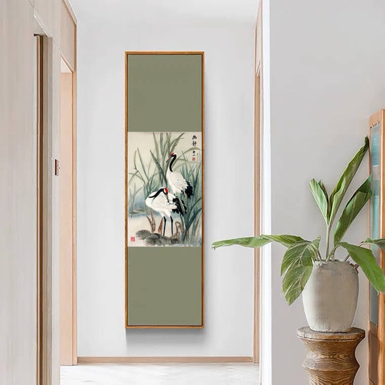 Puede incluir: Una pintura enmarcada de dos grullas blancas de pie en un pantano con juncos verdes. La pintura est&aacute; en un marco marr&oacute;n claro y tiene un fondo verde. Las grullas se miran y tienen marcas negras en sus alas y cabezas. La pintura tiene caracteres chinos en la esquina superior derecha.