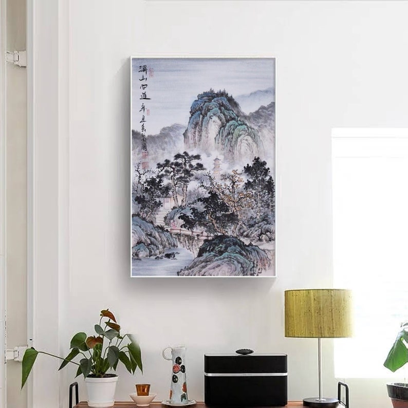 May include: A black and white painting of a mountain landscape with a river flowing through it. The painting is framed in a white frame and is hanging on a white wall. The painting is titled "雪山" in Chinese characters.