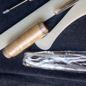 Peut inclure: Un ensemble d'outils de couture comprenant une bobine de fil beige, une petite paire de ciseaux et un outil en plastique blanc avec une aiguille.
