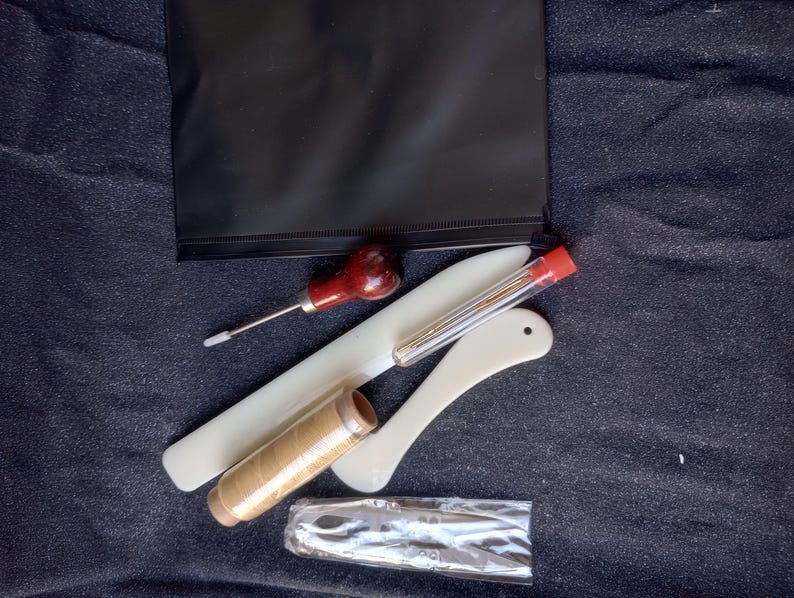 Peut inclure: Une trousse de maroquinerie avec des outils et des fournitures. La trousse comprend un poin&ccedil;on en cuir, un chevalet de couture, un tube d'aiguilles, une bobine de fil cir&eacute; et une pochette zipp&eacute;e noire.