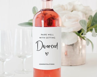 Może przedstawiać: Biała etykieta na butelkę wina z czarnym tekstem, który brzmi "Pairs well with getting Divorced" z małym symbolem serca i tekstem "Congratulations!" na dole.
