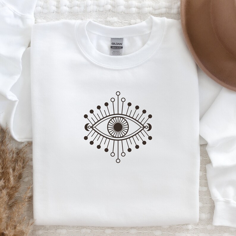 May include: White sweatshirt with a black and white graphic of an evil eye with a sunburst design.