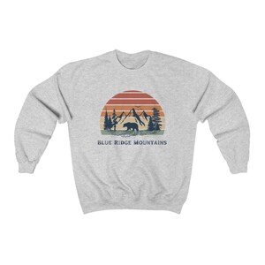 May include: A gray sweatshirt with a vintage-style graphic of mountains, a bear, and a sunset. The text "BLUE RIDGE MOUNTAINS" is printed below the graphic.