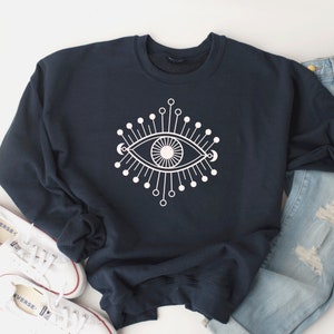 May include: A navy blue sweatshirt with a white graphic of a stylized eye with radiating lines and dots.