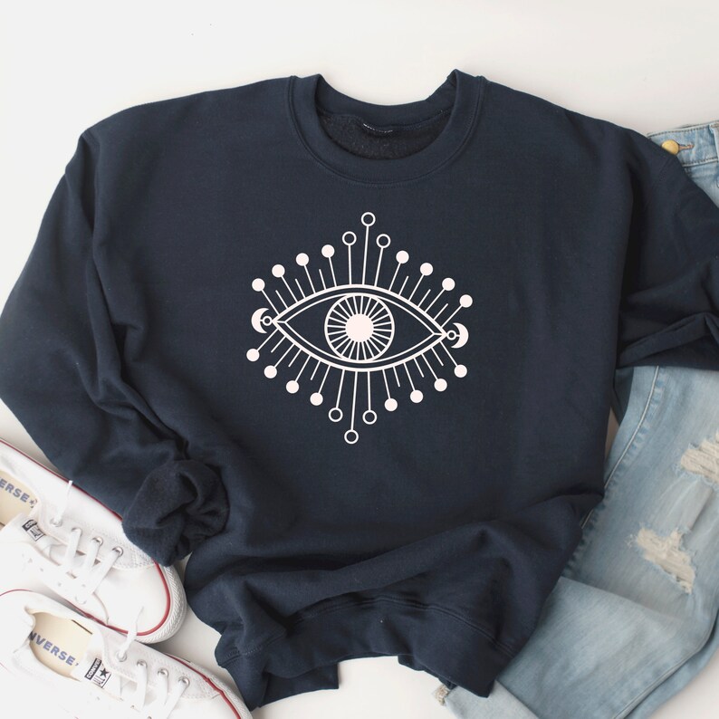 May include: A navy blue sweatshirt with a white graphic of a stylized eye with radiating lines and dots.