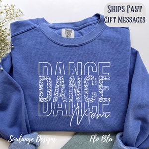 Peut inclure: Un sweat-shirt bleu avec l'inscription "Dance Mom" imprim&eacute;e en blanc avec un motif l&eacute;opard. Les mots sont superpos&eacute;s.