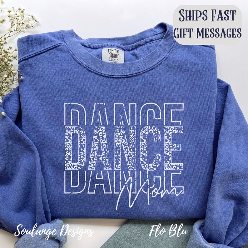 Peut inclure: Un sweat-shirt bleu avec l'inscription "Dance Mom" imprim&eacute;e en blanc avec un motif l&eacute;opard. Les mots sont superpos&eacute;s.