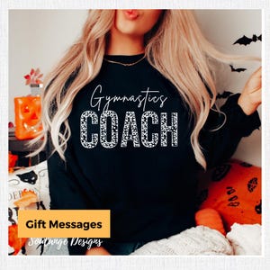 May include: Black sweatshirt with white text that says "Gymnastics COACH" in a leopard print font.