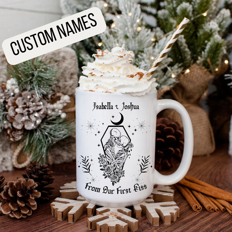 K&ouml;nnte beinhalten: Eine wei&szlig;e Keramiktasse mit einer schwarz-wei&szlig;en Illustration von zwei Skeletten, die sich in einem Sarg k&uuml;ssen. Die Tasse ist mit dem Text "Isabella & Joshua" und "From Our First Kiss" bedruckt.