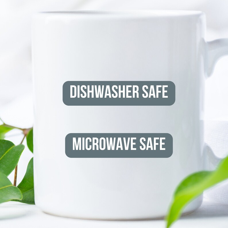 K&ouml;nnte beinhalten: Wei&szlig;e Keramiktasse mit dem Text "Dishwasher Safe" und "Microwave Safe" in grau gedruckt.