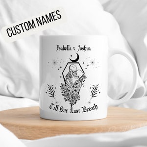 K&ouml;nnte beinhalten: Wei&szlig;e Keramiktasse mit einem schwarzen Design von zwei Skeletten, die sich in einem Sarg umarmen, mit dem Text "Isabella & Joshua Till Our Last Breath" und einem Halbmond dar&uuml;ber.