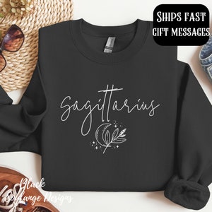 Puede incluir: Sudadera negra con texto blanco que dice "Sagitario" y una luna creciente con un dise&ntilde;o de hoja.
