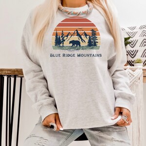 May include: A gray sweatshirt with a vintage-style graphic of mountains, a bear, and a sunset. The text "BLUE RIDGE MOUNTAINS" is printed below the graphic.