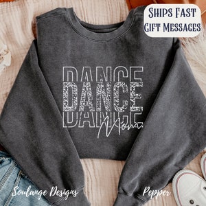 Peut inclure: Un sweat-shirt gris fonc&eacute; avec les mots "DANCE DANCE MOM" en blanc avec un motif l&eacute;opard sur le deuxi&egrave;me "DANCE".